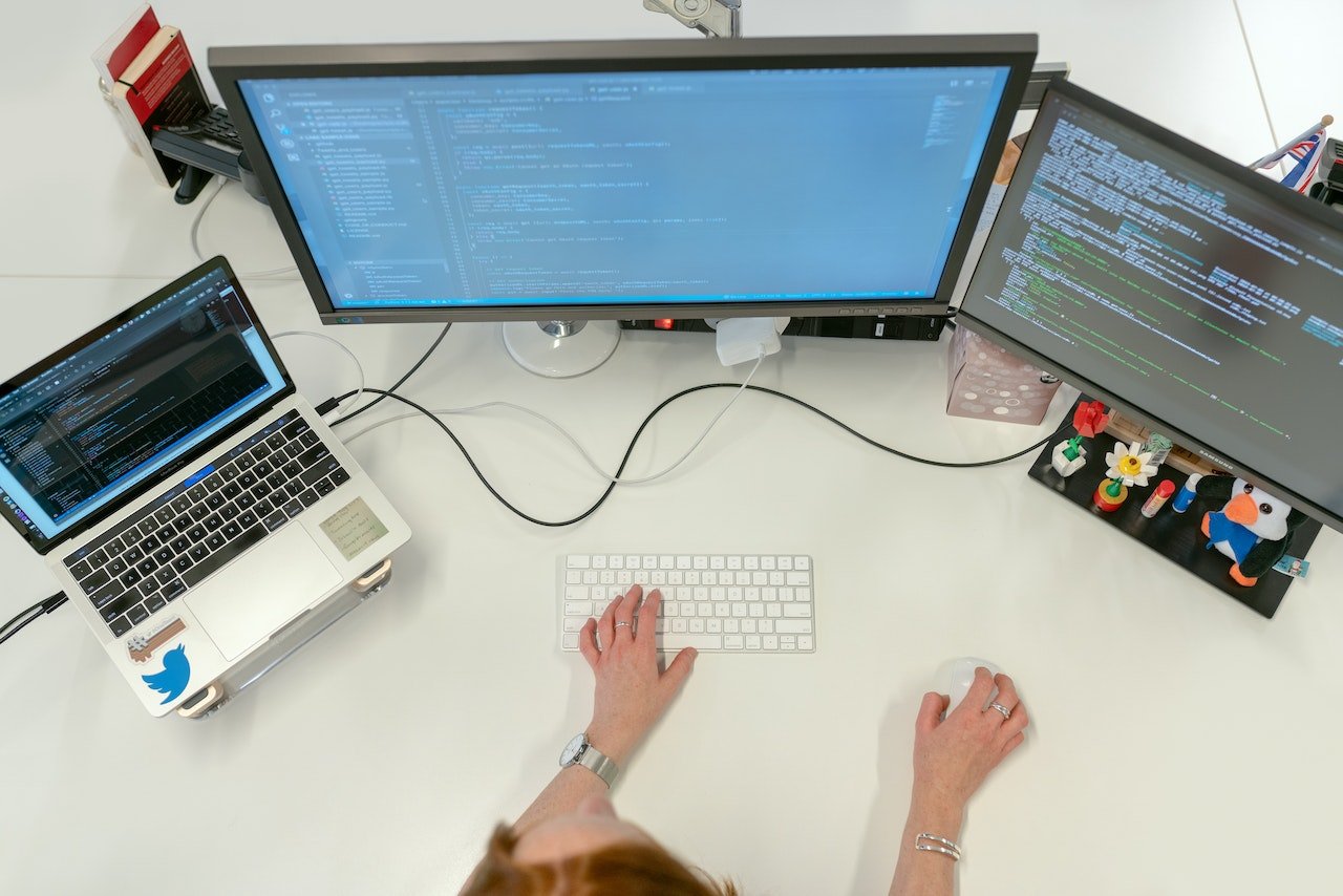 Female tech worker writing code on three screens